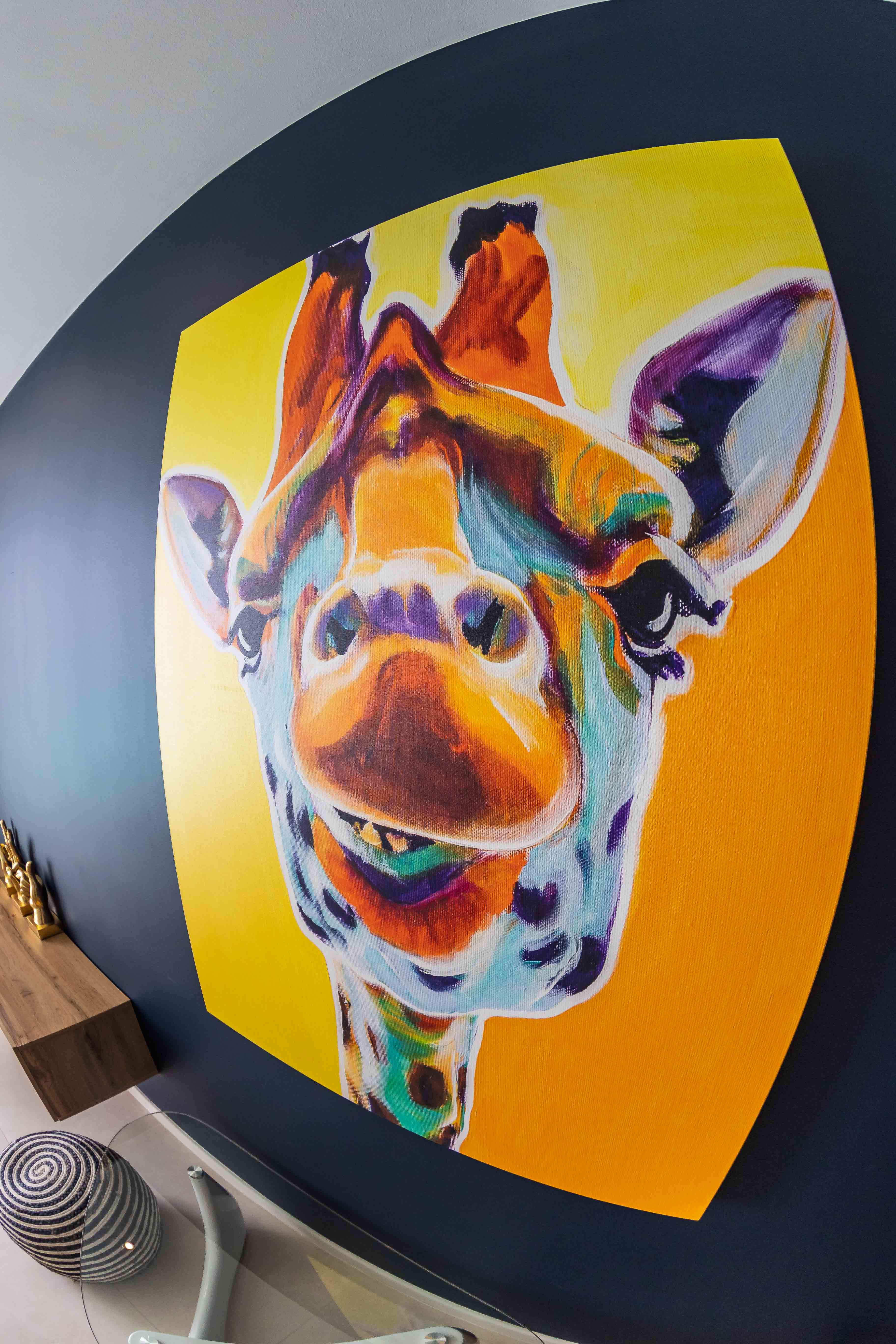 Large colorful pop art giraffe painting on a dark navy curved wall in a luxury Bonaire villa, highlighting the modern interior design and custom artwork.